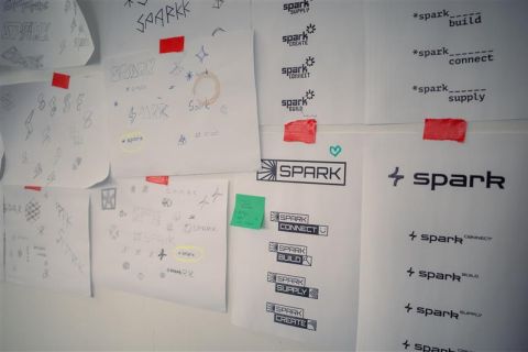 Diverse Zettel mit handschriftlich gestalteten SPARK Logoideen h&auml;ngen an einer Wand.