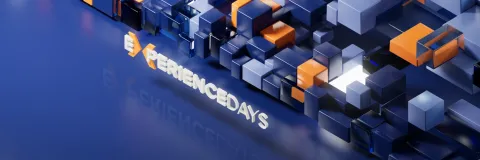 "3D-Rendering mit blauen und orangefarbenen geometrischen Bl&ouml;cken. Der Schriftzug 'EXPERIENCEDAYS' ragt aus der Oberfl&auml;che heraus und spiegelt sich leicht auf dem gl&auml;nzenden, blauen Untergrund.