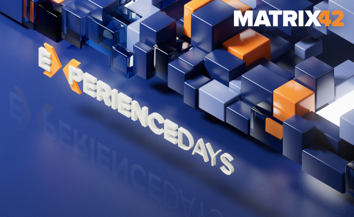 3D-Visual mit blauen und orangefarbenen geometrischen Blöcken. Der Schriftzug 'EXPERIENCE DAYS' ragt aus der glänzenden blauen Oberfläche hervor und reflektiert leicht. Oben rechts das Logo 'MATRIX42'.